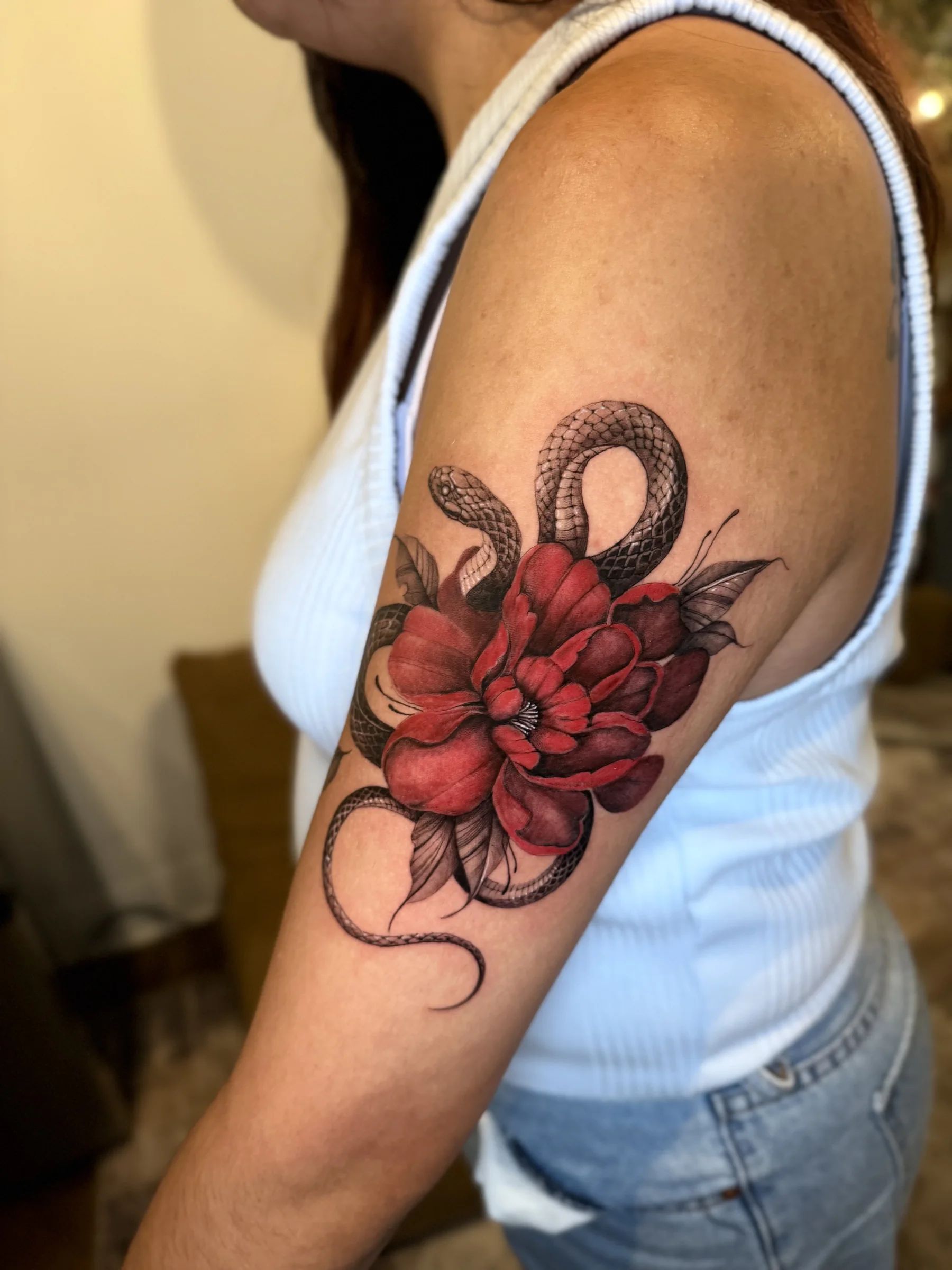 Snake coiled through a red peony on an upper arm
