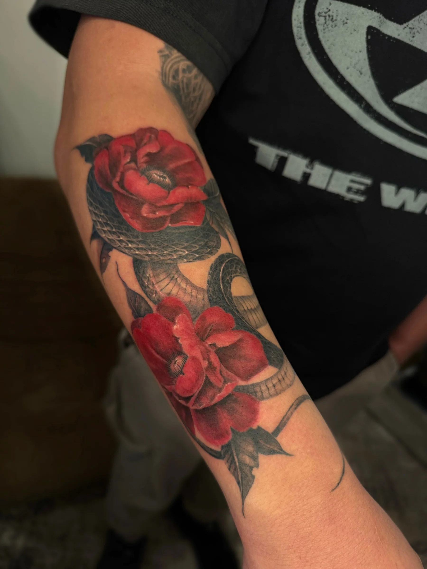 Snake and red roses tattooed down a forearm