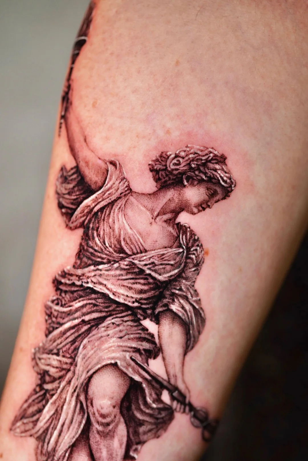 Winged statue tattoo down an upper arm